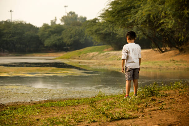 Rear view of boy standing at riverbank while exploring nature
