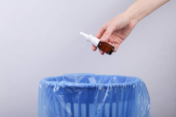 istock Hand throws nasal spray bottle into trash bin with package on gray background 1357010032