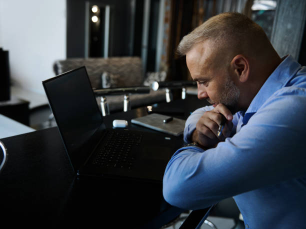 istock Handsome middle aged entrepreneur, charming European man, freelancer sitting with thoughtful look in front of a laptop at home 1357013399