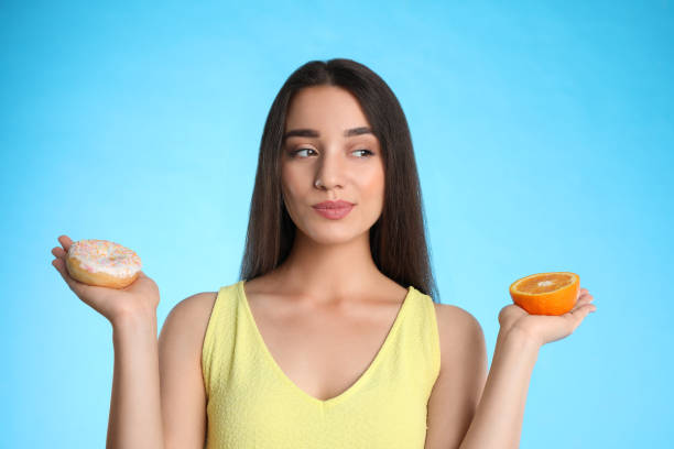istock Woman choosing between orange and doughnut on light blue background 1357016207