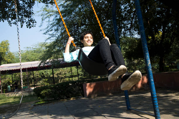 istock Happy girl sitting on swing at park 1357016283