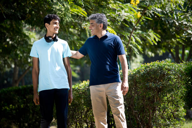 Carefree father with teenage son spending leisure time at park Carefree father with teenage son spending leisure time at park indian man walking in park stock pictures, royalty-free photos & images