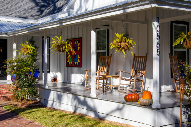 Hanging ferns, wooden rocking chairs, colorful art, and a collection of pumpkins create an inviting seasonal look for the front porch of a renovated wood-frame house in historic White Springs, Florida stock photo