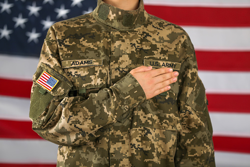 Female American soldier holding hand over heart with flag of USA on background, closeup. Military service