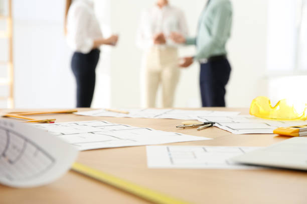 istock Colleagues in office, focus on table with construction drawings and tools 1357023981