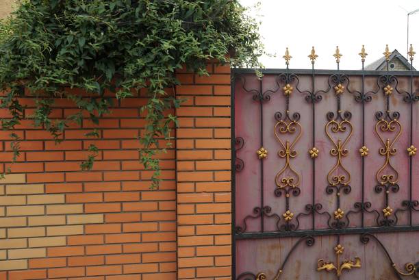 part of a red metal gate with a forged pattern and a brick wall of a fence in green vegetation on the street