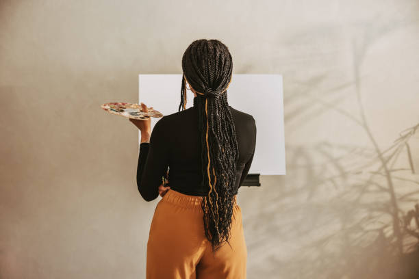 creative young woman holding a palette in an art studio - women artist painting easel imagens e fotografias de stock