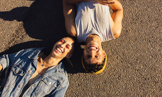 High angle view of two happy friends lying down on the road. Two youngsters smiling cheerfully while lying outdoors under the sun. Best friends of the opposite sex having fun together.