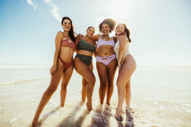 istock Happy female friends standing on beach water 1357042087