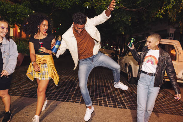 Vibrant young man showing his friends some moves Vibrant young man showing his friends some dance moves at night. Group of happy young people walking together while holding beer cans. City friends having a good time on the weekend. drink can photos stock pictures, royalty-free photos & images