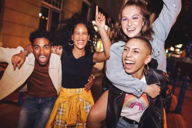 Excited young woman piggybacking her best friend outdoors at night. Happy young women having fun while going out with their friends in the city. Vibrant friends spending their weekend together.