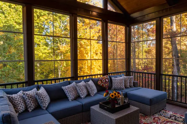Cozy screened porch in early morning, rain drops on window and autumn leaves and woods in the background.