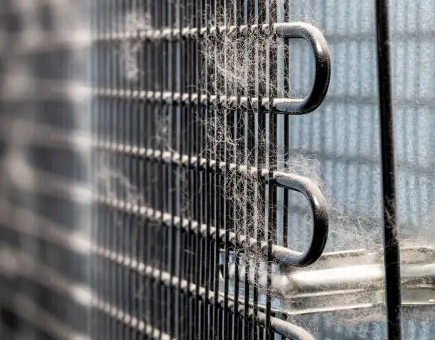 Photo of Dirty coolant tubes and radiating fins at the back of a fridge.