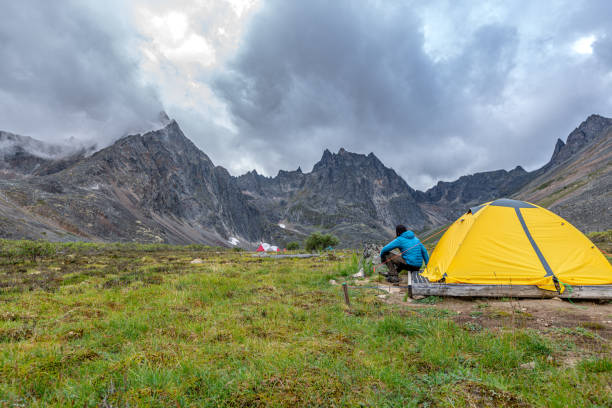 Hiker sitting beside a small tent in backcountry campground.