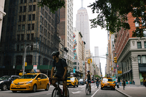 Fifth avenue in New York City with cars, yellow taxis and cyclist. The Empire State Building and nearby skyscrapers are in the background. View from the Fifth Avenue and W26th street nearby Madison Square Park