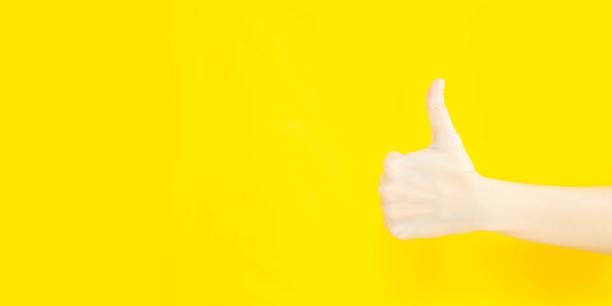 istock woman's hand with thumbs up gesture  in copy space area for advertisement promotion or text on a yellow background 1357058735