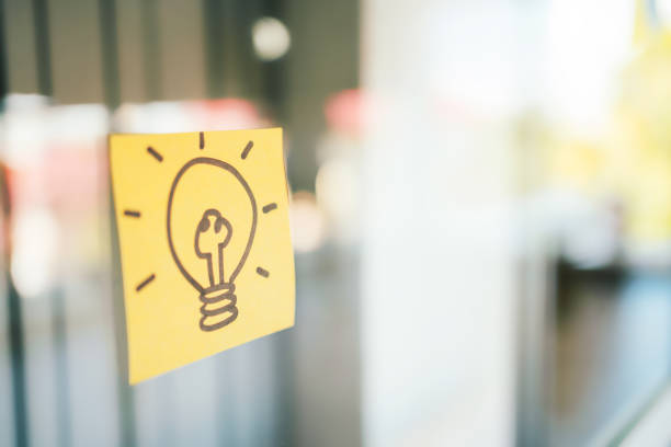 istock Hand drawing light bulb that draws on a yellow sticky note on glass board with copy space. 1357059388