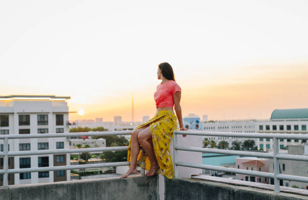 istock Young woman on a rooftop overlooking a city at sunset 1357060916