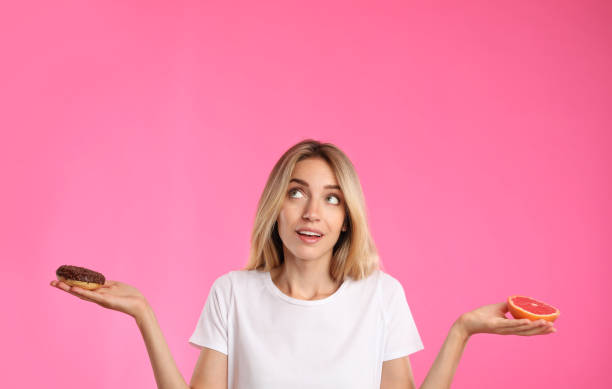 istock Woman choosing between doughnut and healthy grapefruit on pink background 1357070729