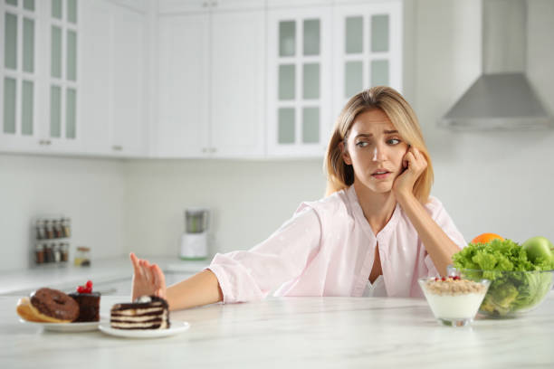istock Woman choosing between sweets and healthy food at white table in kitchen 1357071034