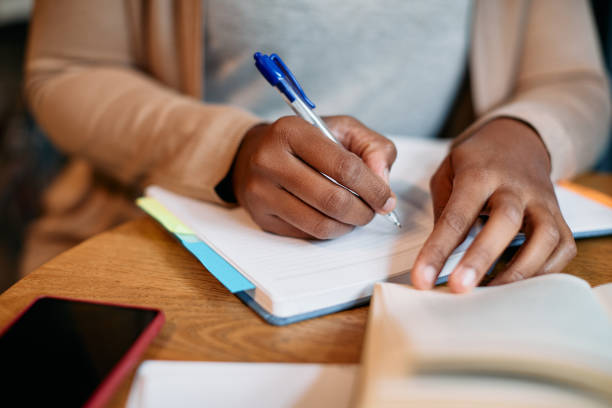 istock Close-up of black female student writing in notebook while learning in library, 1357073729