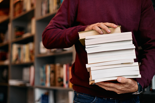 Hombre irreconocible sosteniendo una pila de libros mientras estudia en una biblioteca. photo