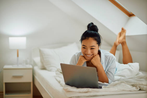 istock Happy Asian woman using laptop while relaxing in her bedroom. 1357073867