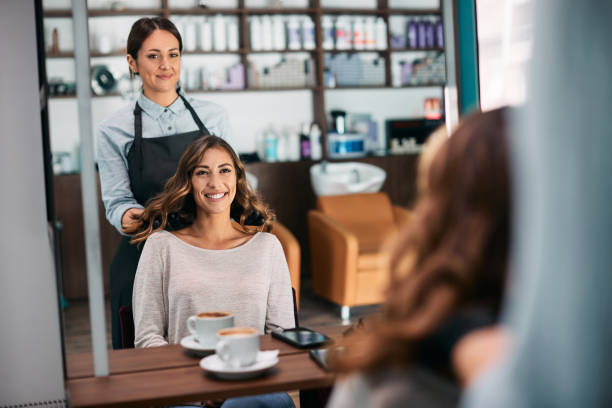 Reflection in a mirror of happy woman and her hairdresser after hair treatment at the salon. Young woman feeling satisfied while looking herself in a mirror after getting her hair styled at hairdresser's. salon mirror stock pictures, royalty-free photos & images