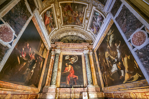 Rome, Italy, November 30 -- The Contarelli Chappel with the triptych of paintings on the life of Saint Matthew by Michelangelo Merisi da Caravaggio, inside the church of San Luigi dei Francesi (St. Louis of the French), in the historic and baroque heart of Rome. Built between 1518 and 1589 by the architects Giacomo Della Porta and Domenico Fontana, the church was consecrated on 8 October 1589. This Catholic temple is the national church in Rome of France, dedicated to the figure of King St. Louis IX. Caravaggio painted this triptych between 1599 and 1600, illustrating The Vocation of Saint Matthew (left), The Inspiration of Saint Matthew (center) and The Martyrdom of Saint Matthew (right). In 1980 the historic center of Rome was declared a World Heritage Site by Unesco. Super wide angle and high definition image.