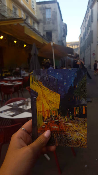 Vincent Van Gogh's Cafe Terrace at Night Hand of a woman showing a postcard depicting the Cafe Terrace at Night painted by Vincent Van Gogh. In the background, the bar located at the Place Lamartine in Arles vincent van gogh painter photos stock pictures, royalty-free photos & images