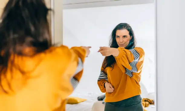 Photo of Self confident single woman pointing finger at her reflection in mirror, dancing and felling good