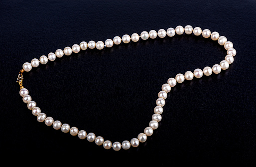 Pearl beads on a dark leatherette surface with space for text. Close up.