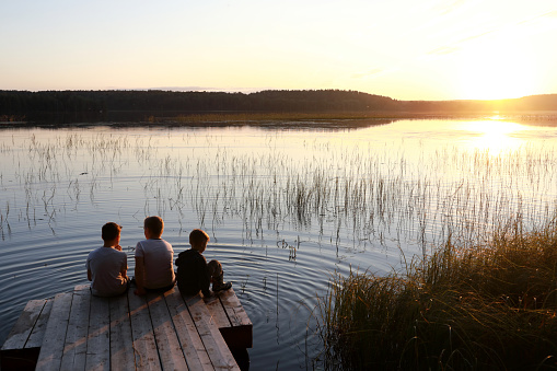 Children sitting on wooden bridge by lake at sunset, Karelia