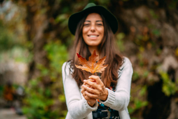 Beautiful young woman in forest throwing leaves on autumn day
