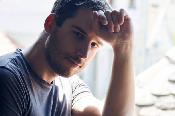 istock Portrait of young man sitting at window 1357096347