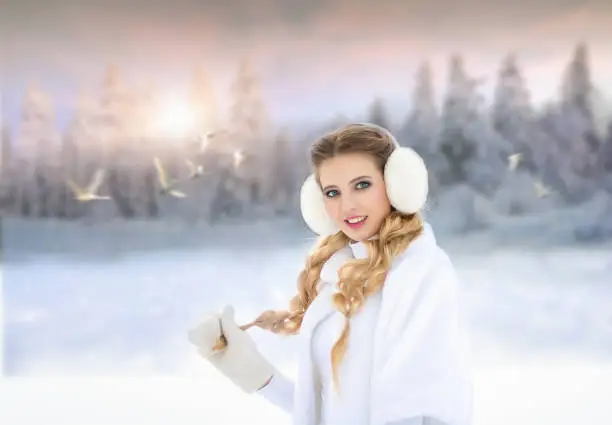 Photo of Young blonde woman in white clothes in winter looking at white flying swans in the sky in the background smiling. Swan Lake.