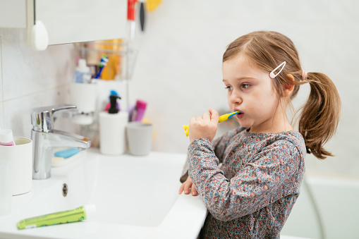 Little girl brushing her teeth, rinsing, washing hands and face in bathroom