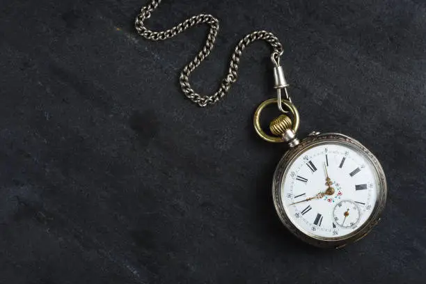 Vintage antique pocket watch with chain on a dark stone background