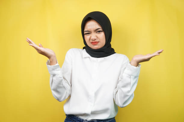 Beautiful asian young muslim woman with i don't know sign expression, isolated on yellow background stock photo
