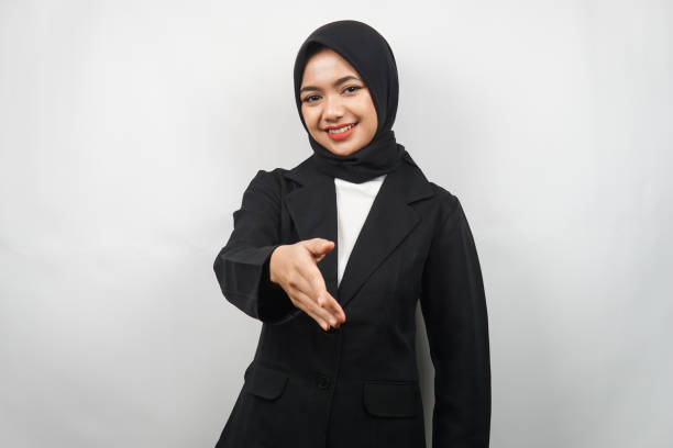 beautiful young asian muslim business woman confident and smiling, with hands shaking the camera, hands sign of cooperation, hand sign of agreement, hand sign of friendship, isolated on gray background - japanese ethnicity women asian and indian ethnicities smiling imagens e fotografias de stock