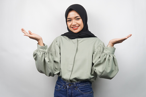 Beautiful young asian muslim woman confident and smiling, with open arms, presenting something, presenting product, isolated on gray background