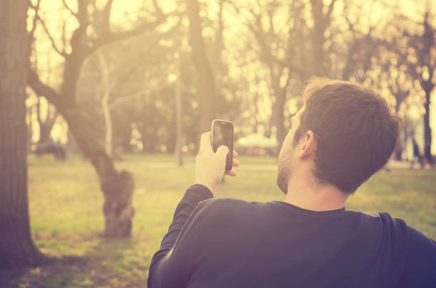 istock Young man sitting in the park and texting a message 1357104513