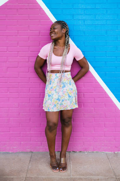 Very happy black African woman posing on a wall in many colors. Lifetyle photo of a happy African woman Cheerful african-american woman in colorful skirt against a multicolored wall. Woman with braids standing on one leg and arms outstretched looking to the side. Concept of people. black hair braiding stock pictures, royalty-free photos & images