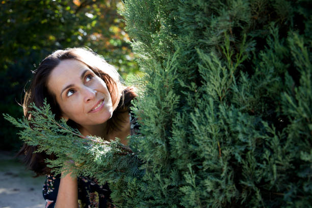 woman hiding behind a cypress branch looking up