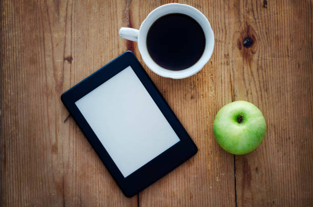 E-book reader, green apple and coffee cup on wooden table