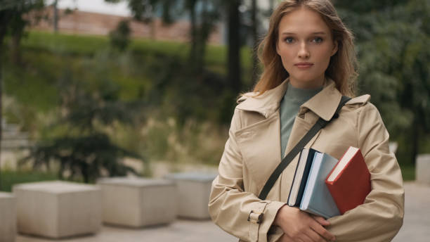 istock Attractive stylish student girl standing with textbooks looking confident in camera going to college through city park 1357112885