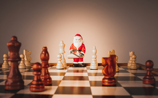 Figurine of Santa Claus between chess pieces on a chessboard.