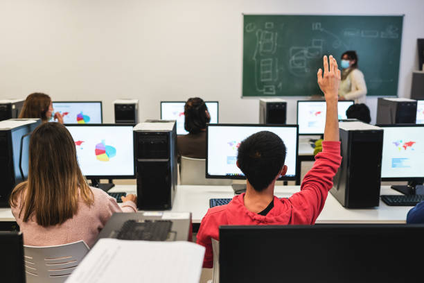 Rear view of large group of students having a class at computer lab.