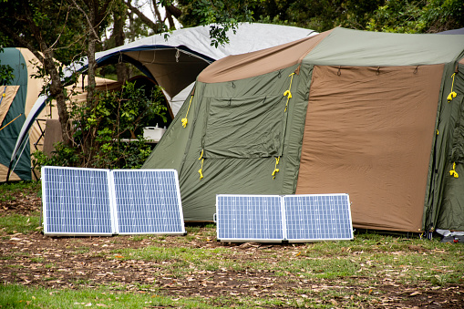 Portable foldable solar panels and Tent at the campsite surrounding by nature. Camping and recreation concept