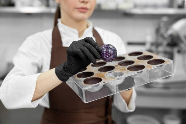 Close-up, a female pastry chef takes out a handmade chocolate candy from a polycarbonate mold Close-up, a female pastry chef takes out a handmade chocolate candy from a polycarbonate mold chocolate truffle making stock pictures, royalty-free photos & images